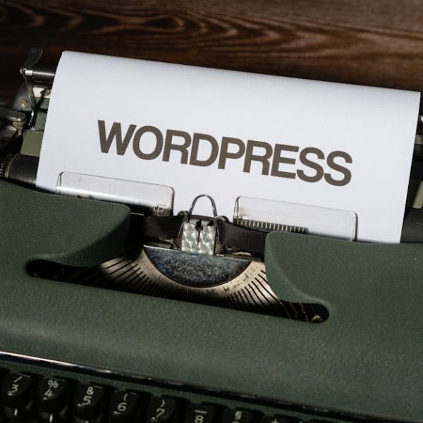 A sheet of paper with the word "WORDPRESS" typed on it is loaded in a vintage green typewriter on a wooden surface.