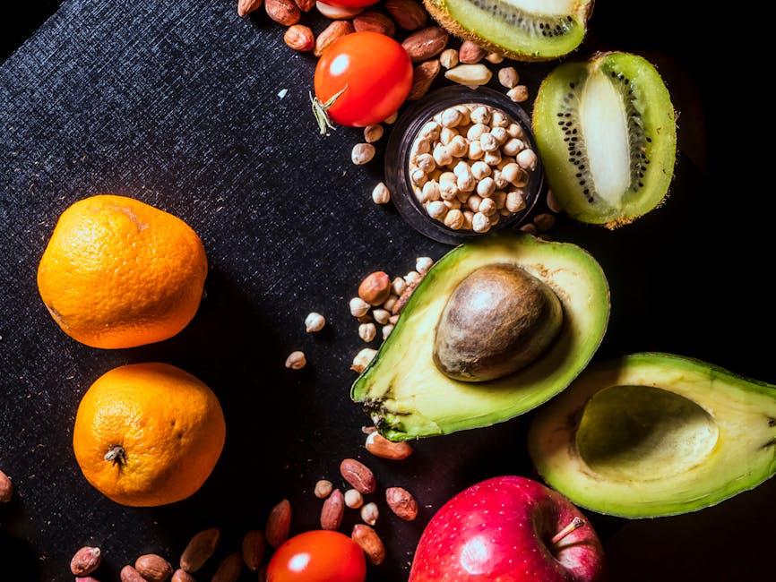 Assorted fruits and nuts, including tangerines, apple, avocado, kiwi, cherry tomatoes, peanuts, and chickpeas, arranged on a black surface.