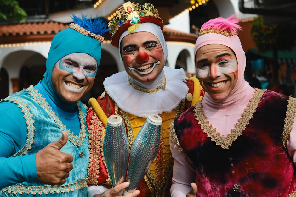 Three smiling clowns in colorful costumes and makeup pose together, with one clown holding juggling pins. Two clowns give thumbs up.