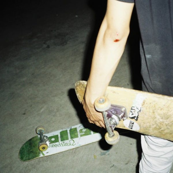 Person with a scraped elbow holds a skateboard while another skateboard lies on the ground, both on a concrete surface at night.