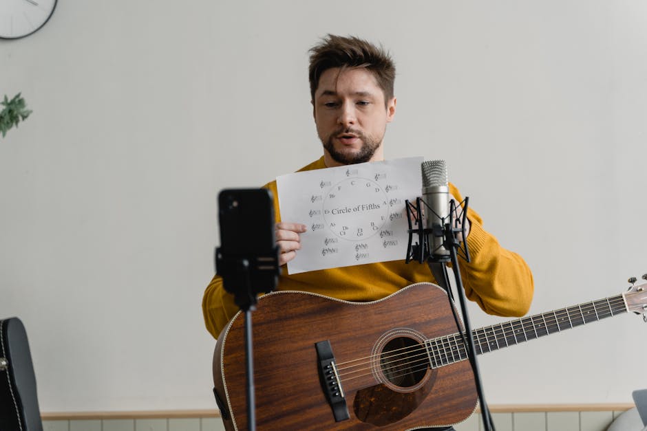 A man holding a guitar displays a sheet labeled "Circle of Fifths" in front of a microphone and smartphone on a stand.