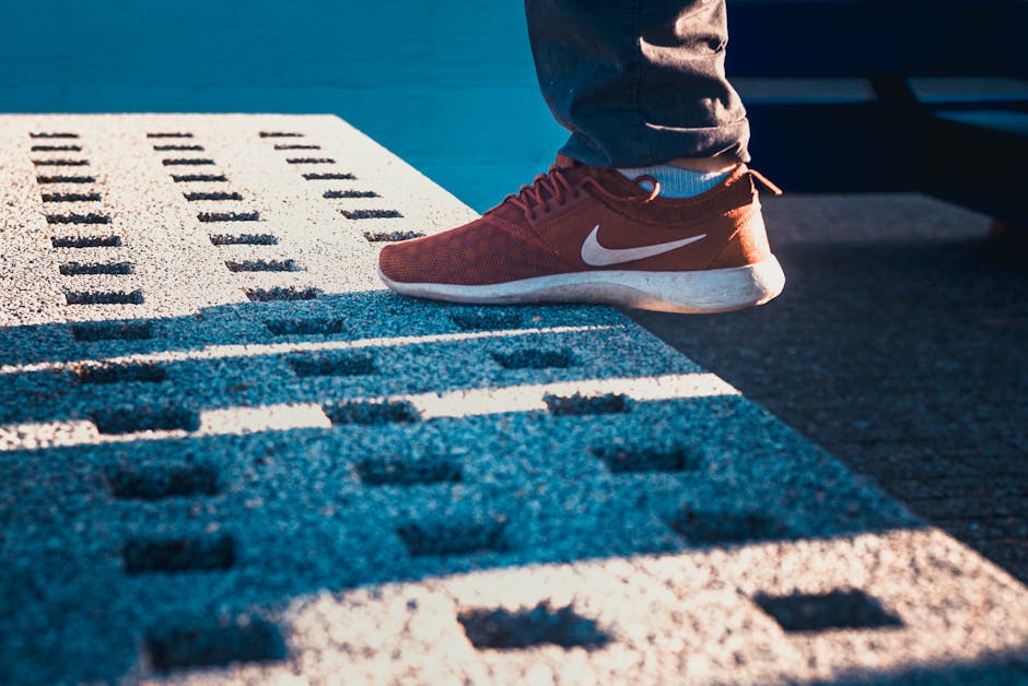 A person wearing red Nike sneakers stands on a textured, perforated concrete surface in sunlight.