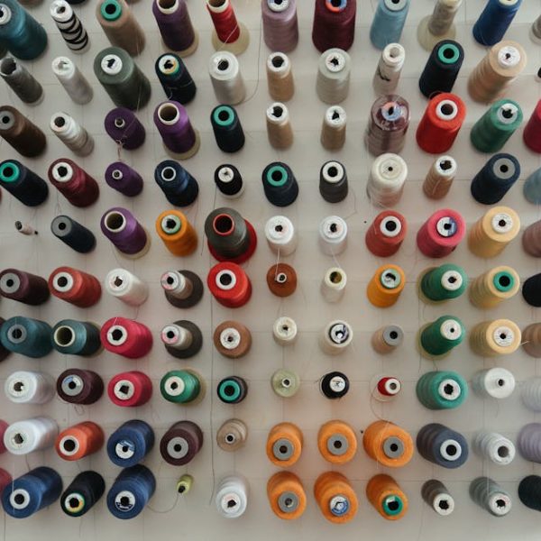 A top-down view of multiple colorful spools of thread arranged neatly in rows on a white surface.