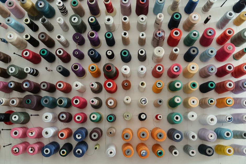 A top-down view of multiple colorful spools of thread arranged neatly in rows on a white surface.