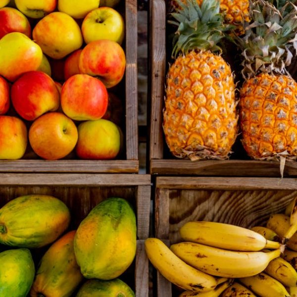 Four wooden crates display a variety of fruits: apples in the top left, pineapples in the top right, papayas in the bottom left, and bananas in the bottom right.