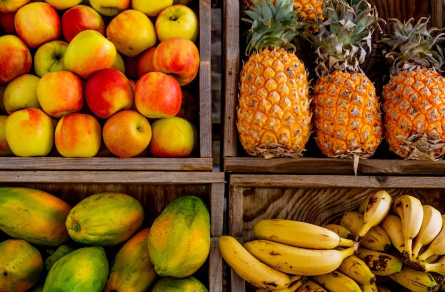Four wooden crates display a variety of fruits: apples in the top left, pineapples in the top right, papayas in the bottom left, and bananas in the bottom right.