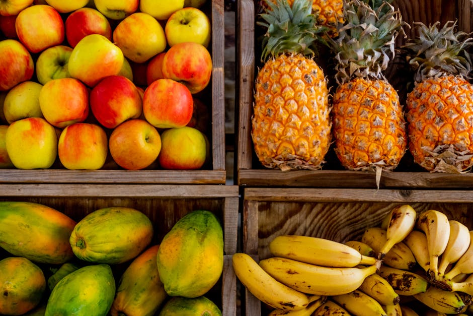 Four wooden crates display a variety of fruits: apples in the top left, pineapples in the top right, papayas in the bottom left, and bananas in the bottom right.