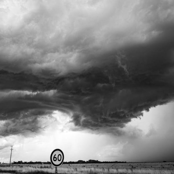 Dark storm clouds gather over an open field with a 60 km/h speed limit sign in the foreground.