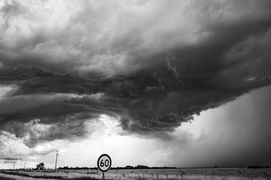 Dark storm clouds gather over an open field with a 60 km/h speed limit sign in the foreground.