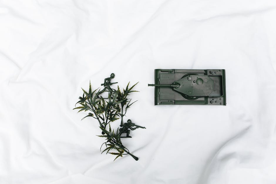 Plastic toy soldiers and a toy tank are arranged on a white surface next to a small artificial plant.