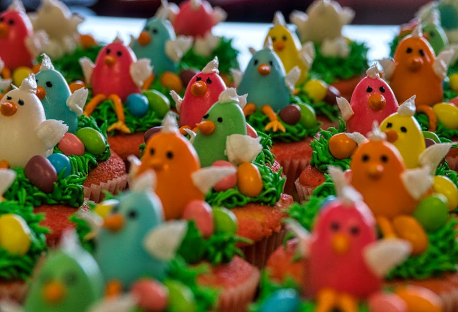 Colorful cupcakes decorated with icing birds and eggs, arranged closely together on a tray.