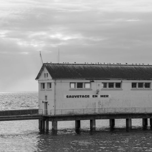 A white coastal building labeled "SAUVETAGE EN MER" stands on stilts above the water, with a cloudy sky and calm sea in the background.
