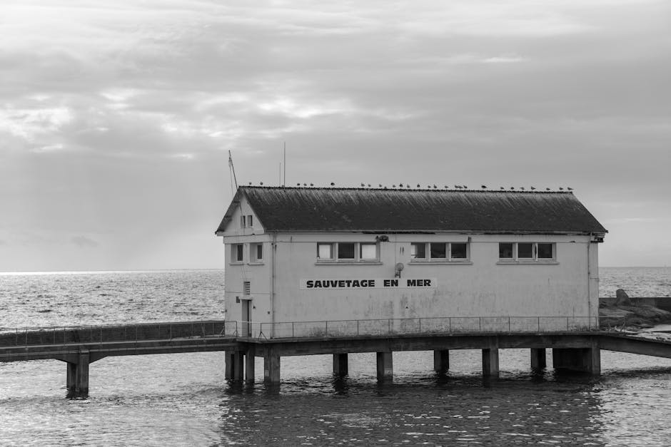 A white coastal building labeled "SAUVETAGE EN MER" stands on stilts above the water, with a cloudy sky and calm sea in the background.