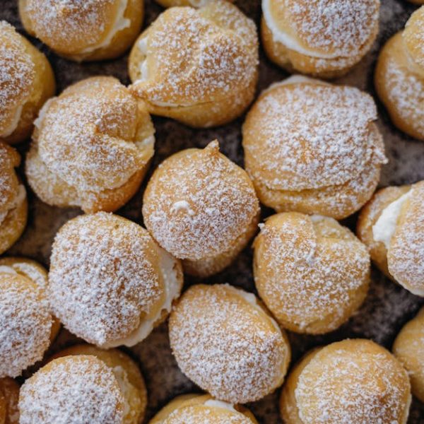 A close-up view of multiple cream puffs topped with powdered sugar, arranged closely together.