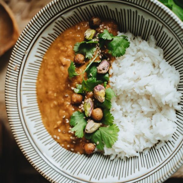 A bowl with white rice and chickpea curry topped with cilantro and seeds, placed on a wooden surface.