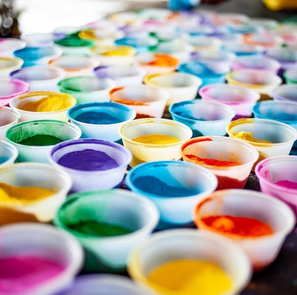 Rows of small plastic cups filled with various colors of powdered pigment are arranged on a table.