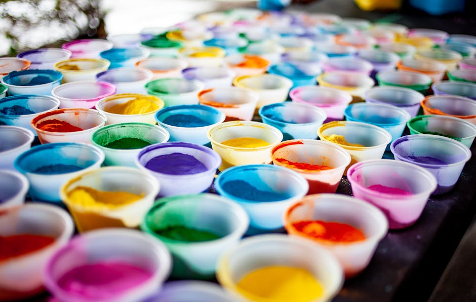 Rows of small plastic cups filled with various colors of powdered pigment are arranged on a table.