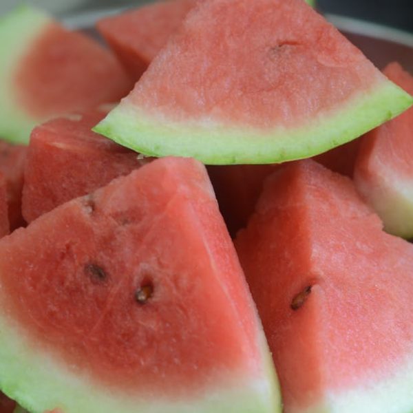 A close-up of several triangular slices of watermelon with green rinds, arranged in a bowl.