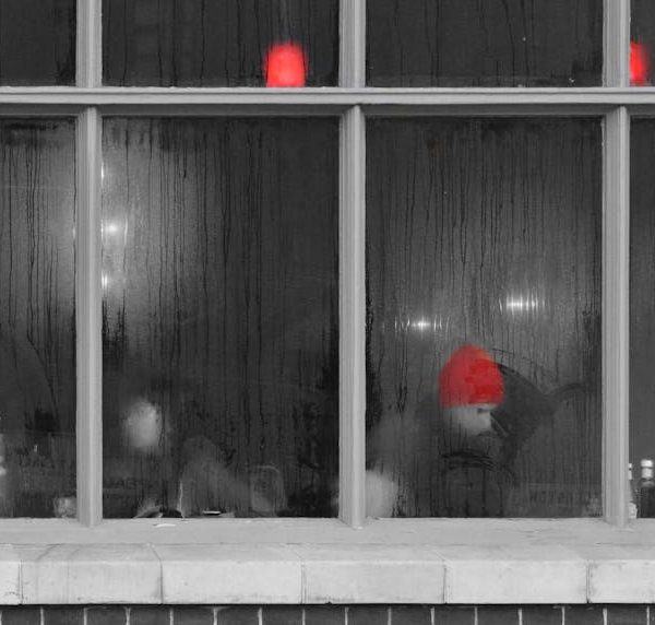 People are sitting inside a foggy-windowed cafe; one person is wearing a bright red hat while red lights are glowing above.