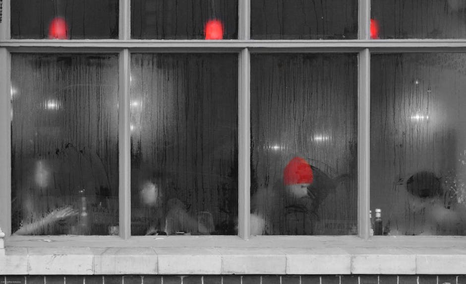 People are sitting inside a foggy-windowed cafe; one person is wearing a bright red hat while red lights are glowing above.