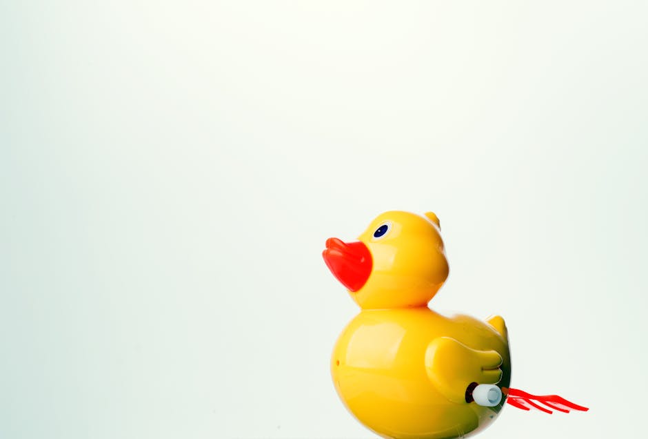 A yellow plastic wind-up toy duck with a red beak is set against a plain, light background.