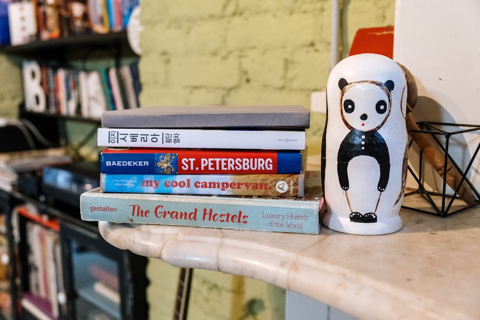 A stack of five travel books sits on a marble surface next to a painted panda figurine, with shelves and books in the blurred background.
